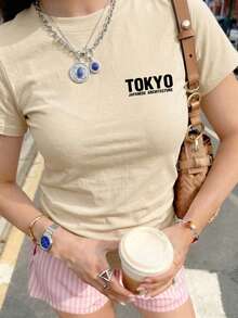 女士杏色短袖T恤，采用耐磨面料，背面印有东京古建筑和黑色花卉拼贴图案，展现日式极简街头风，适合城市漫步、艺术展览和旅行摄影。休闲夏季之选。 - 杏色 - 查看 3