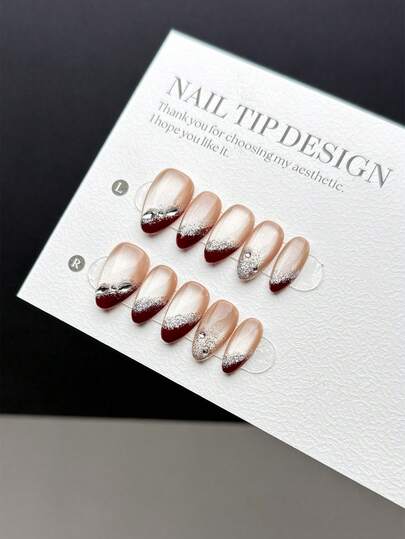 10片纯手工制作的按压式美甲贴片，短款杏仁形，风格轻盈奢华，简约时尚。它融合了红色法式美甲和裸色烟火猫眼效果，并饰以银粉和水钻。这是一款高端美甲按压式美甲配件，适合女士和女孩日常佩戴，并附赠美甲套装。