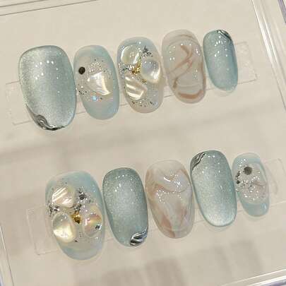 10片纯手工制作的按压式美甲贴片，短款椭圆形，以蓝色猫眼为底，浅蓝色和银色搭配贝壳3D纹理，珍珠和闪粉装饰，呈现梦幻、透明而活泼的外观。温柔优雅可爱的美甲贴片，适合女士和女孩春夏秋冬各种节日派对和日常生活使用。
