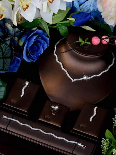 一套银色立方氧化锆（CZ）首饰套装，包括长方形切割CZ波浪形项链、配套水滴耳环、波浪形戒指和波浪形网球手链，抛光闪亮，适合女性日常佩戴和休闲聚会。