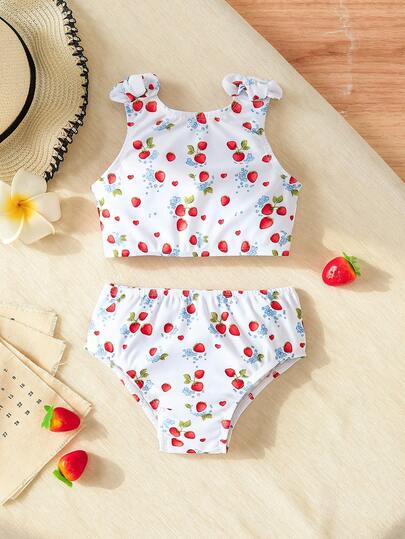 Traje de baño de dos piezas para niña pequeña, diseñado para bebé y niña pequeña, con un estilo fresco y dulce con base blanca, estampado de fresa y detalles florales azules, creando un efecto visual alegre y lindo. Adopta un diseño de dos piezas, la parte superior tiene un estilo de manga de volantes con decoración de lazo en los tirantes, añadiendo un toque delicado; la Bottom es en estilo de pantalones cortos triangulares, que se ajusta bien al bebé. Adecuado para usar en la piscina, la playa y otros escenarios.