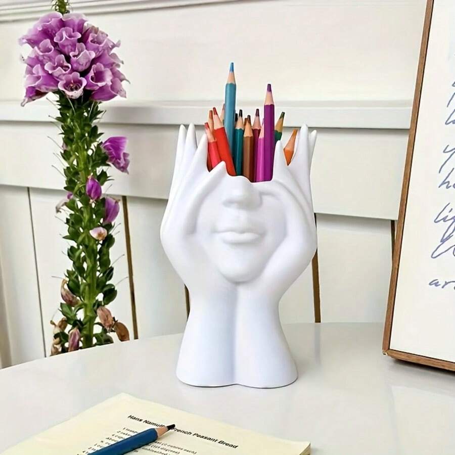 1 Hộp đựng cọ trang điểm hình mặt người màu đen/trắng. Thiết kế tối giản màu trắng tái hiện vẻ thư thái của một khuôn mặt tựa vào tay, đóng vai trò như một vật trang trí nghệ thuật trên bàn làm việc.