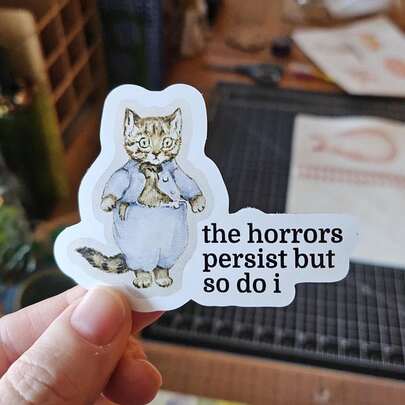 1PC 3 Inch Removable Waterproof Outdoor PVC Vinyl Decal Cute Cat In Blue Pajamas "The Horrors Persist But So Do I" Dark Humor Resilience Meme Viral Gen Z Mental Health Quote Kawaii Aesthetic Perfect For Laptop Phone Water Bottle Skateboard Helmet Journal Car Bumper Notebook Dorm Decor Travel Luggage Ideal Gift For Teens Girls Boys Overthinkers Burnout Survivors Ages 13-30 Creative Decorative Sticker Waterproof Vinyl Decal For Any Smooth Surface