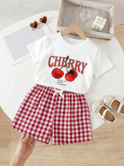 Bộ 2 món cho bé gái, gồm áo thun ngắn tay in chữ hình quả anh đào và quần short kẻ caro nhiều màu sắc có nơ trang trí, thích hợp mặc hàng ngày, đi chơi hoặc nghỉ mát, mùa hè.
