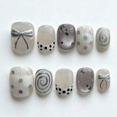 Bộ 10 móng tay này có tên là Silver Bow Dot Swirl. Bộ móng này có sự kết hợp nhẹ nhàng giữa nền trắng sữa và bạc ánh kim, cùng với các họa tiết nơ bạc bóng, chấm bi và các đường xoáy bạc. Lớp sơn bóng bắt sáng như những chiếc nơ bạc, chấm bi và đường xoáy đang nhảy múa trên nền kem, tạo nên một vẻ ngoài retro mát mẻ.