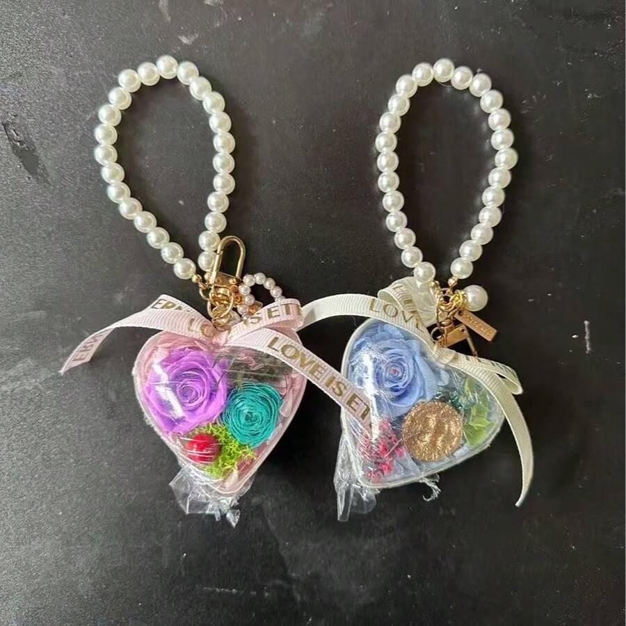 这款精美的手工永生花心形钥匙扣,为您的日常穿搭增添一抹亮色!它以一朵令人惊艳的永生玫瑰为核心,置于透明心形亚克力盒中,搭配优雅的仿珍珠链、精致的缎带和金色五金配件,尽显奢华质感。每一枚钥匙扣都经过精心设计,确保玫瑰花多年保持鲜艳美丽,成为永恒爱情的象征。 - 彩色 - 查看 1
