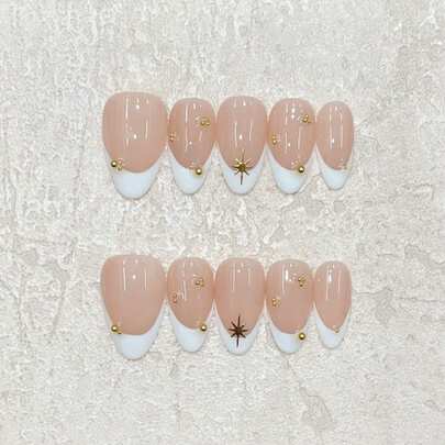Bộ 10 móng tay giả thủ công, móng hình hạnh nhân màu nude, đầu móng kiểu Pháp màu trắng kết hợp với họa tiết ngôi sao vàng và hạt vàng nhỏ, kiểu dáng đơn giản nhưng cao cấp, phù hợp cho đi làm hàng ngày, hẹn hò và dự tiệc. Bộ móng giả thủ công có thể tái sử dụng, bao gồm một tờ keo dán và một dũa móng mini.