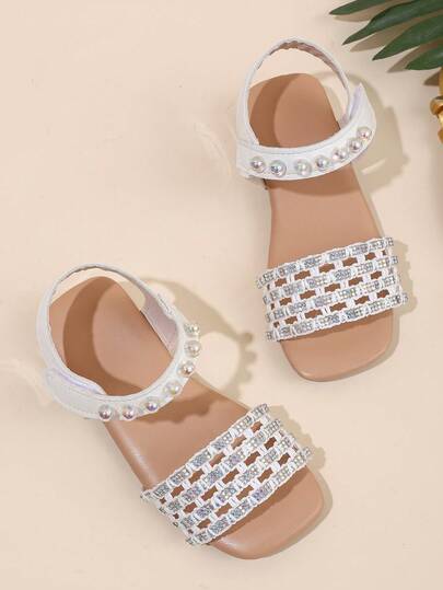 1 đôi sandal bé gái với quai đan họa tiết nước, trang trí hạt cườm óng ánh, chất liệu da mềm mại, mũi vuông, khóa dán, và gót liền hở mũi, thích hợp cho bé mặc đi học hàng ngày và đi chơi trong kỳ nghỉ.