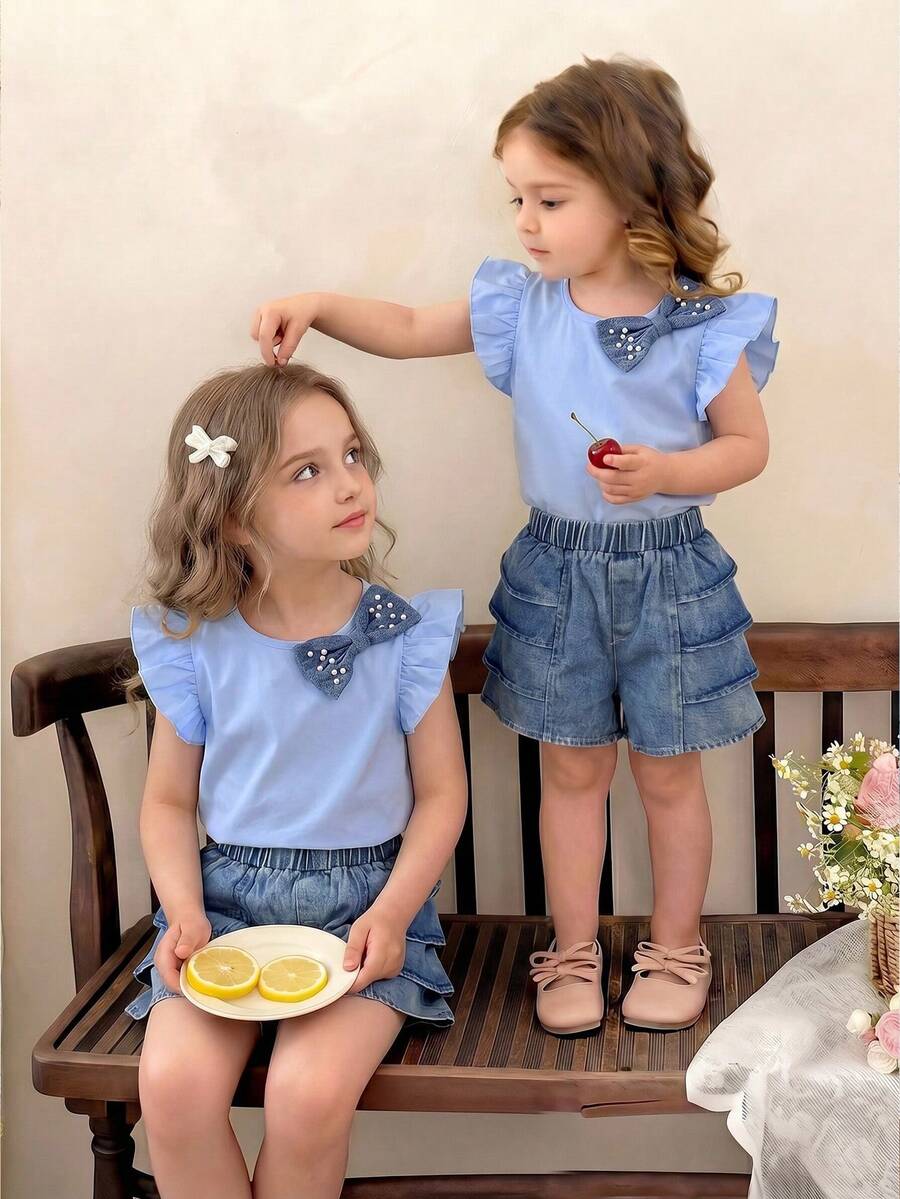 Bộ đồ thể thao thường ngày cho bé gái, gồm áo thun cổ tròn tay ngắn thắt nơ ngọc trai và quần short denim nhiều lớp cạp chun ống rộng. - Màu xanh lam - Xem 1