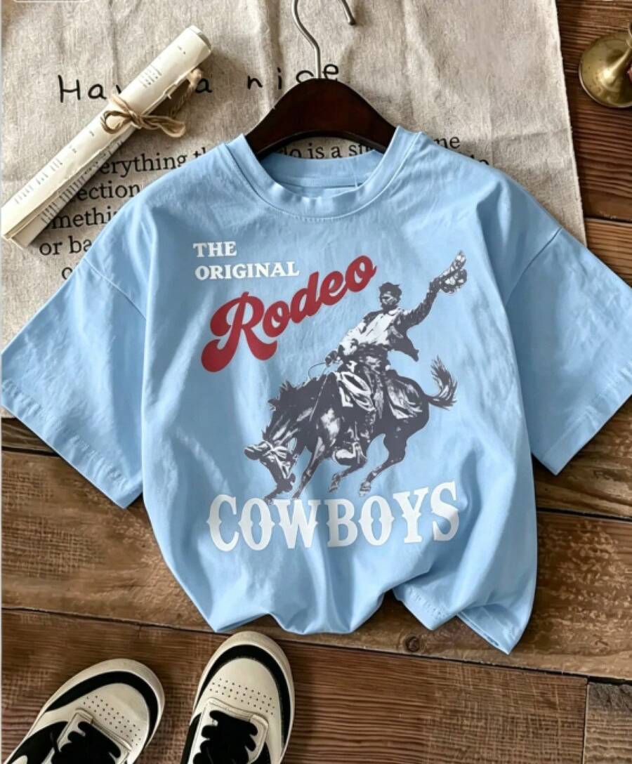Short-Sleeved T-Shirt, Printed With A Design Of A Cowboy Riding A Horse, Combined With The Phrase "THE ORIGINAL Rodeo" And Cowboy Pants, Brown Leather Boots And A Cowboy Hat, Creating A Strong Western Cowboy Style. 100% Cotton - 藍色 - 查看 1
