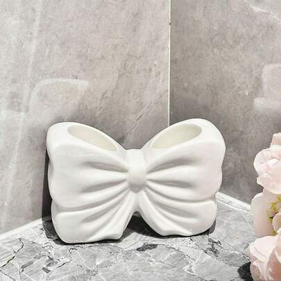 1 chiếc hộp đựng bút bằng gốm hình nơ, đồ dùng văn phòng phẩm dễ thương để trên bàn làm việc.