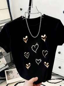 Esta camiseta holgada y transpirable presenta un diseño sencillo con corazones metálicos estampados y detalles de pedrería. Es una camiseta informal adecuada tanto para ocasiones festivas como para el uso diario. - Negro - Ver 1