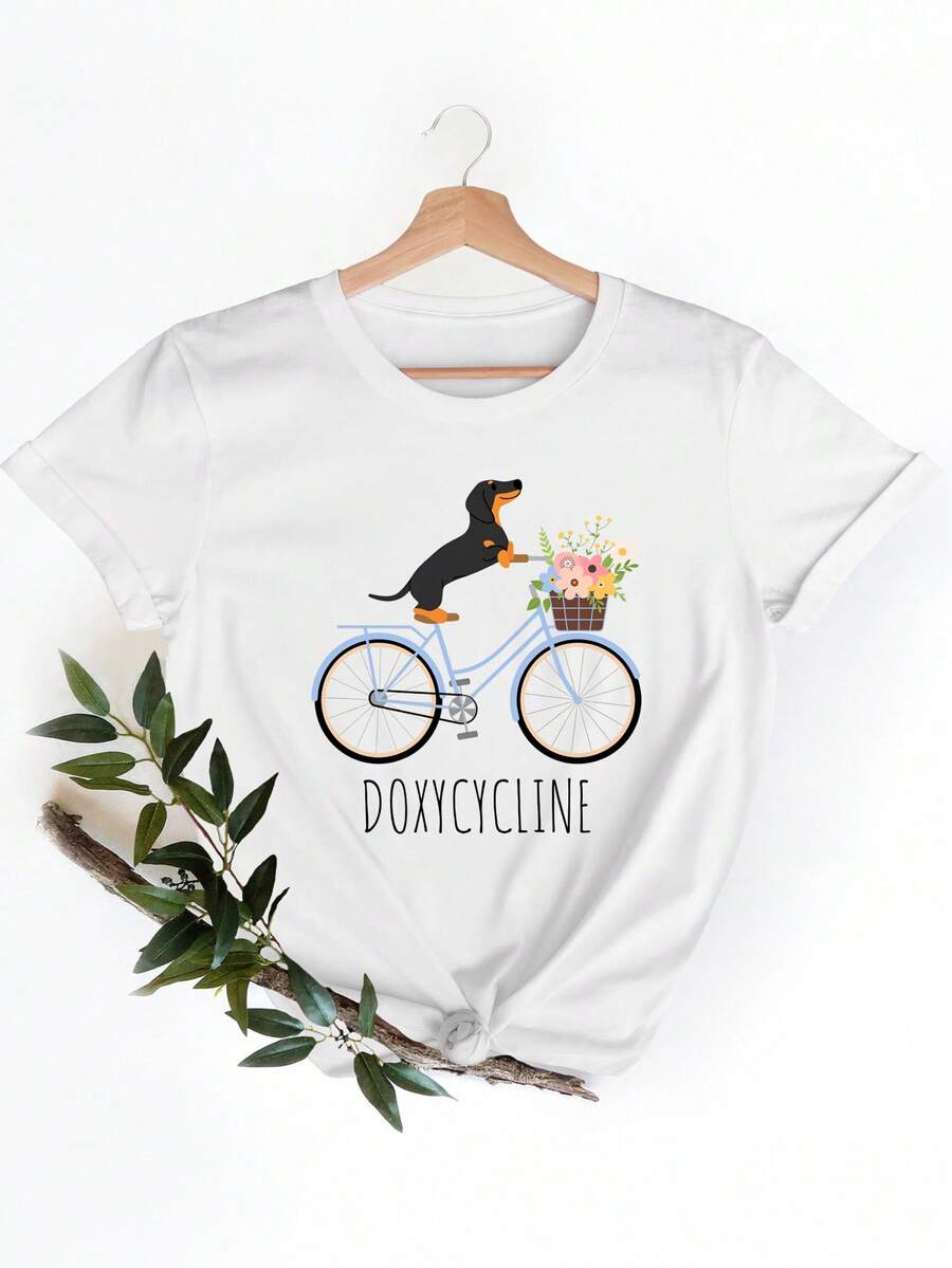 Camiseta de moda de mujer en blanco con una impresión de un Dachshund montando en bicicleta con una cesta de flores, junto con lalabra 'Doxycycline'. I para el uso casual durante las salidas diarias y el ocio
