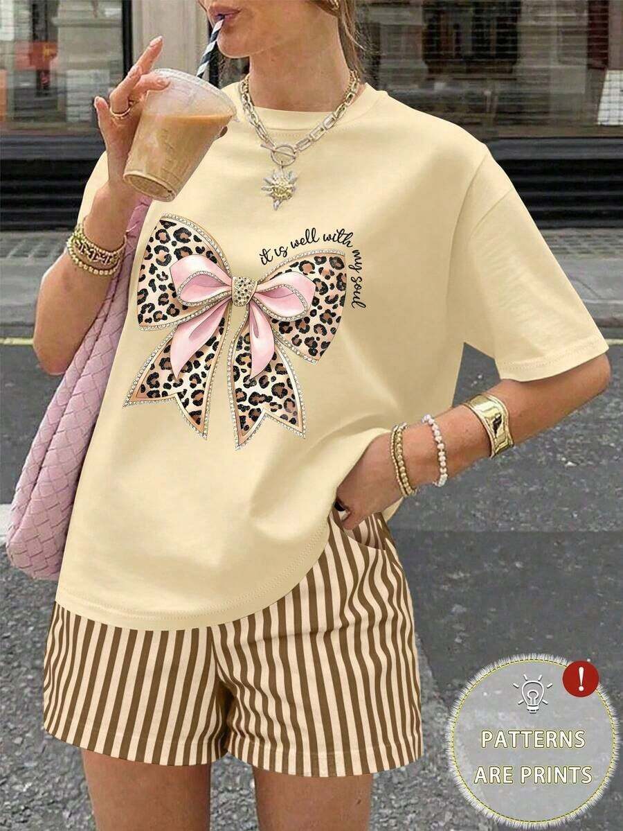 Una camiseta de manga corta para mujer con estilo retro americano, de corte holgado y con diseño estampado (los pantalones son solo para sugerencias de estilo). Esta pieza sencilla y elegante presenta un patrón de letras impresas con temática tropical, lo que la convierte en un elemento imprescindible para crear un look relajado de vacaciones, perfecto para ocasiones como el Día del Trabajo y el Día de la Independencia de México. - Beis - Ver 1