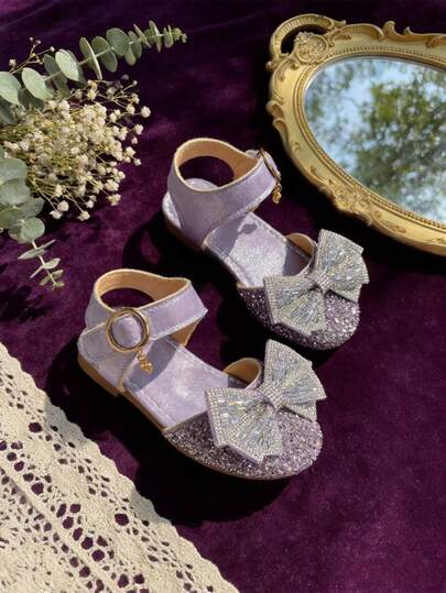 Ein Paar 2026 neue Sommersandalen für Mädchen mit glitzernden Pailletten und Schleifen-Dekorationen. Aus PU-Material gefertigt, sind es flache Prinzessinnenschuhe in einem süßen Lila. Perfekt für Geburtstagsfeiern, Bühnenauftritte und den täglichen Gebrauch.