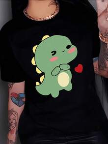 Drawing Of A Small Green Dinosaur With Pink Cheeks Smiling While Holding A Red Heart Expressing Tenderness And Affection. Women's Casual, Modern, And Fun T-Shirt For Everyday Wear. - 黑色 - 查看 1