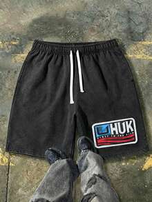 230g Washed Denim Shorts Featuring The Classic HUK Brand Emblem In A Red And Blue Flag-Inspired Color Scheme, With The Brand Slogan "FIRST TO THE FISH" Printed Below. These Men's Retro Washed Denim Shorts Are A Casual, Street-Style Piece Inspired By American Fishing Culture. Comfortable And Breathable, Suitable For Everyday Wear, They Include An Adjustable Drawstring Waist, Elastic Waistband, And Pockets. - Black - View 1