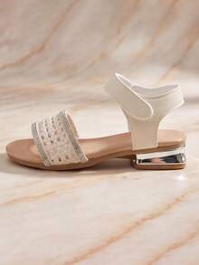 熱銷 3-12 歲兒童輕量白色鏤空編織涼鞋，鏤空編織前帶 + 銀色亮片飾邊 + 魔鬼氈後帶，銀色鏡面低方跟，低調優雅日常風，可搭配白色/米色洋裝、雪紡裙、牛仔短褲、吊帶褲、白色 T 恤日常穿搭 - 米色 - 查看 3