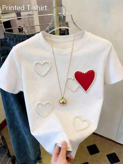 Camiseta de mujer blanca con estampado digital de corazones, diseño con efecto de perlas y corazón rojo, cuello redondo y manga corta, estilo casual dulce y moderno para uso diario.