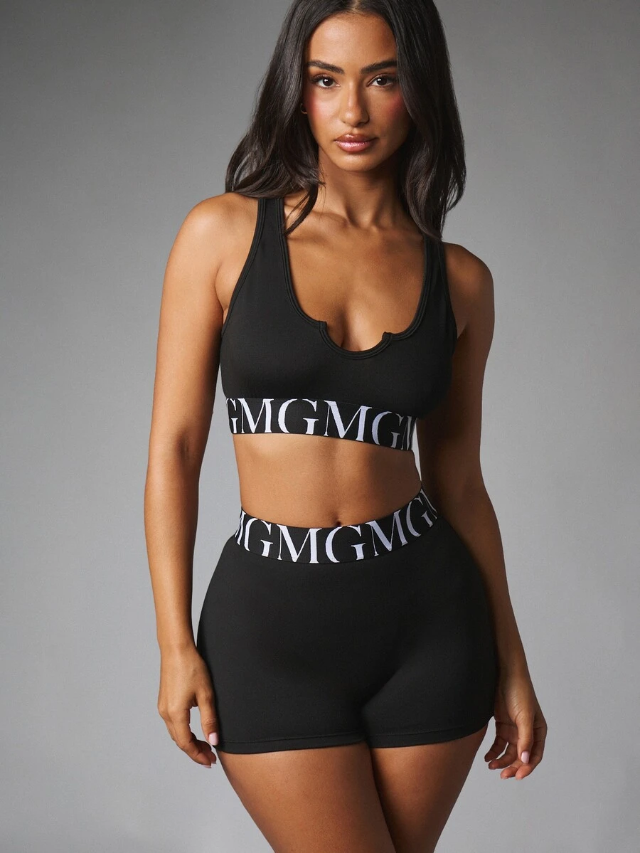 MISSGUIDED طقم ملابس رياضية صيفي من قطعتين GMG بشعار وشريط، حمالة صدر رياضية بظهر متقاطع وشورت دراجة بخصر عالي وحزام مطاطي - الأسود - مشاهدة 1