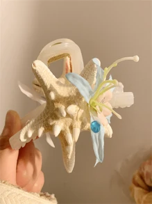 Um novo tipo de presilha de cabelo com flor de concha marinha, adequado para penteados durante férias na praia. Possui um formato de coque que fica na parte de trás da cabeça e vem com uma presilha de cabelo. O adereço de cabeça apresenta um design em forma de tubarão com um lado rosa e um lado azul. É um presente para as senhoras e adequado tanto para uso diário quanto para styling de moda.