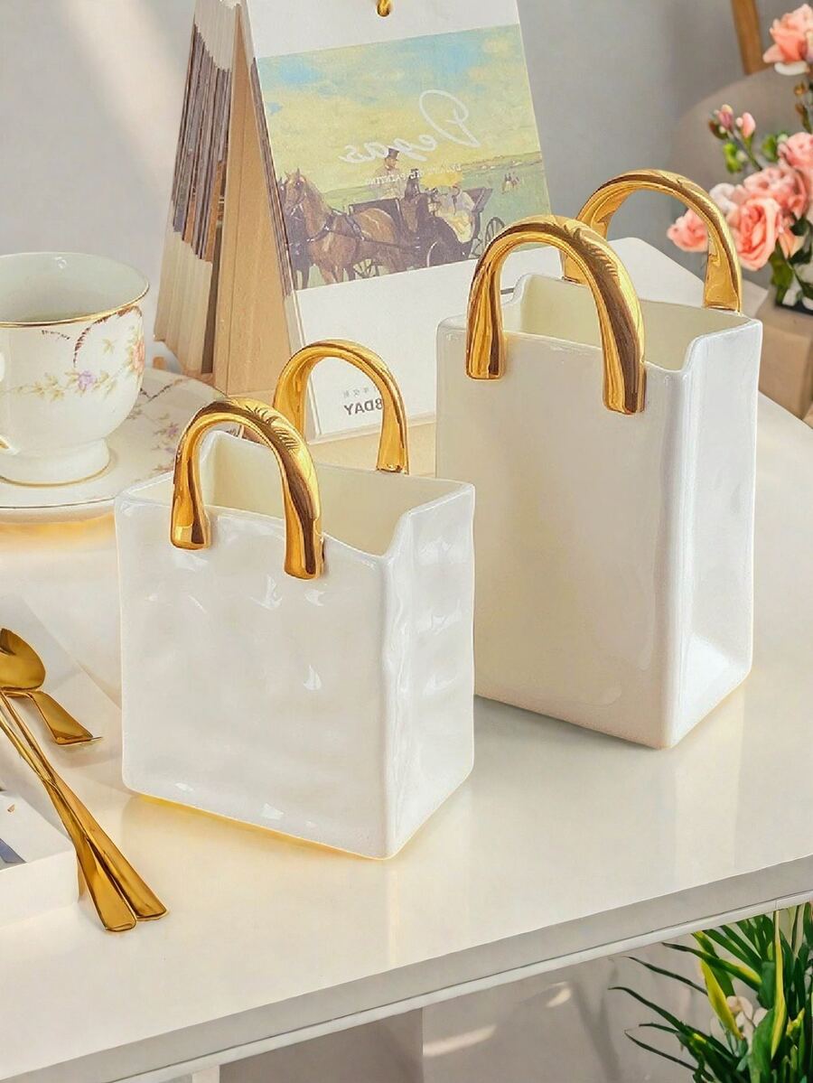 1件独特的白色和金色手提包造型树脂花瓶，这款时尚花瓶配有金属把手，非常适合在咖啡桌、梳妆台上或卧室装饰中展示鲜花，为您的家增添迷人的现代气息。