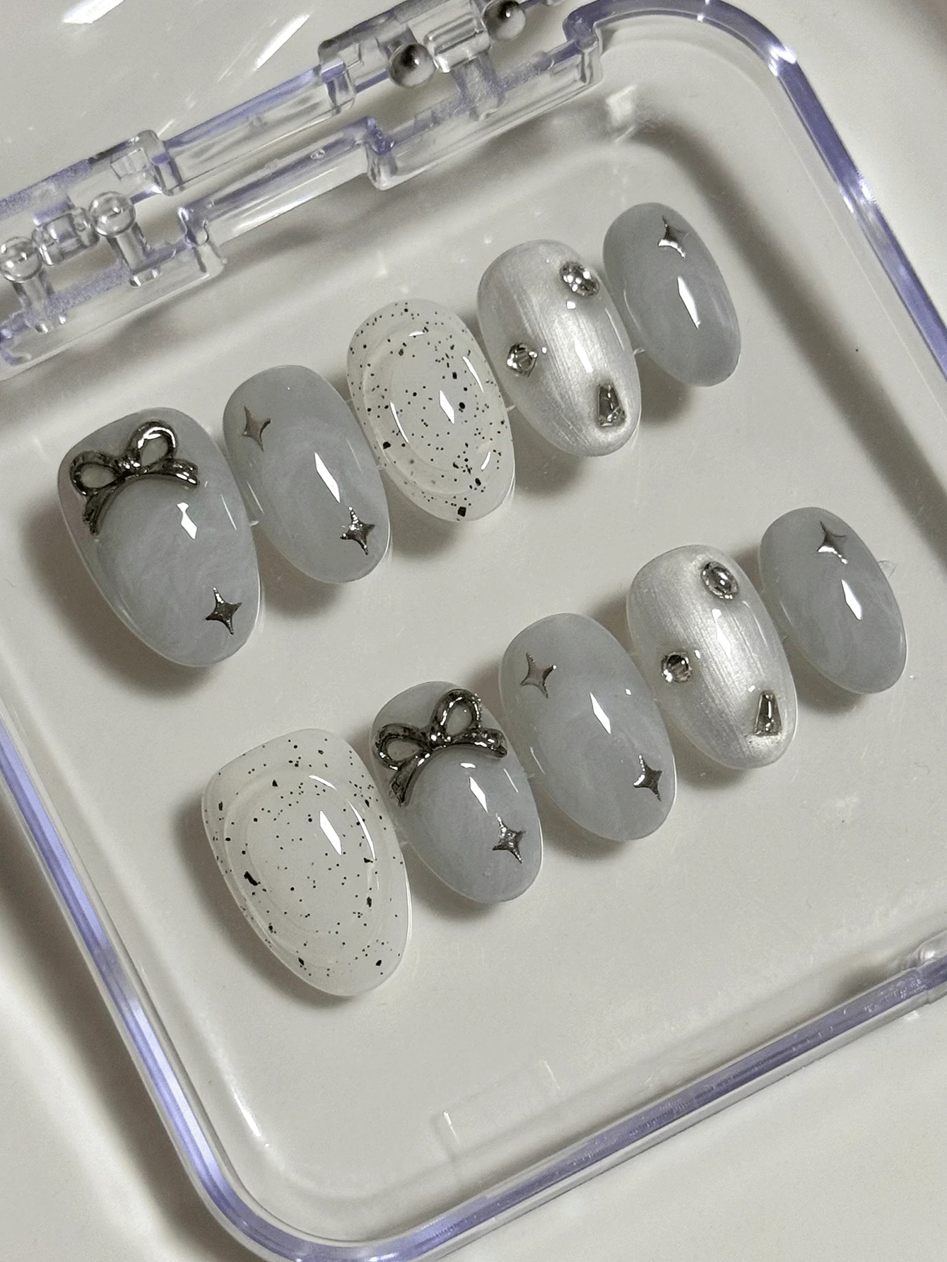 Bộ 10 miếng dán móng tay hình bầu dục màu xám và trắng với các chấm đen không đối xứng, hình ngôi sao, nơ và đá trang trí, mang đến vẻ ngoài nhẹ nhàng và tươi mới, bảo vệ móng tay cao cấp, bộ móng giả có thể tháo rời hoàn chỉnh phù hợp cho các quý cô công sở, sinh viên, các cô gái dự tiệc và mọi mùa, kèm theo 1 lọ sơn gel và 1 dũa móng. - Màu Xám nhạt - Xem 1