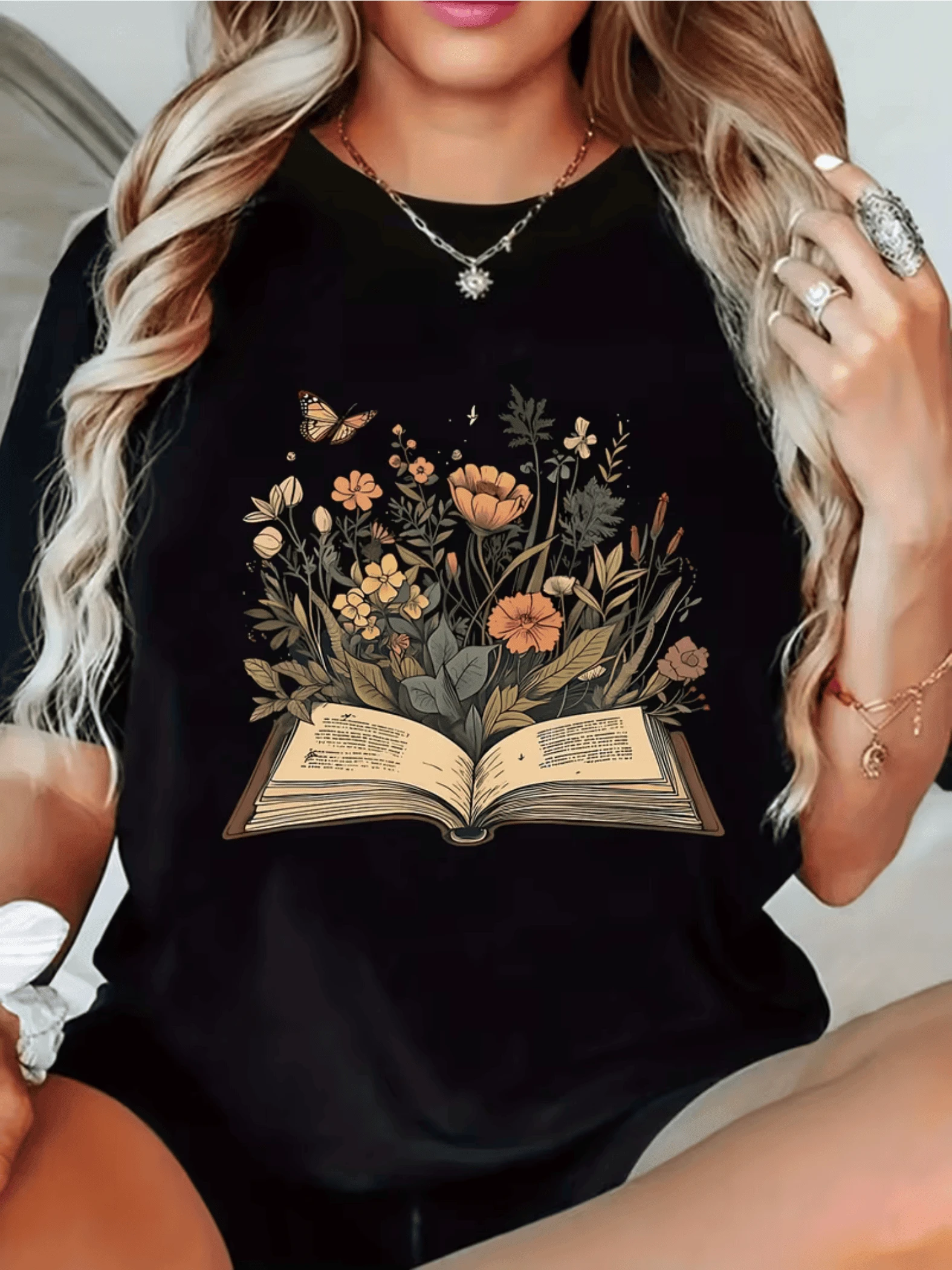 Libro abierto del cual brotan flores silvestres y una mariposa simbolizando el poder del conocimiento que florece en armonía con la naturaleza camiseta de mujer cómoda y moderna perfecta para uso diario - Negro - Ver 1