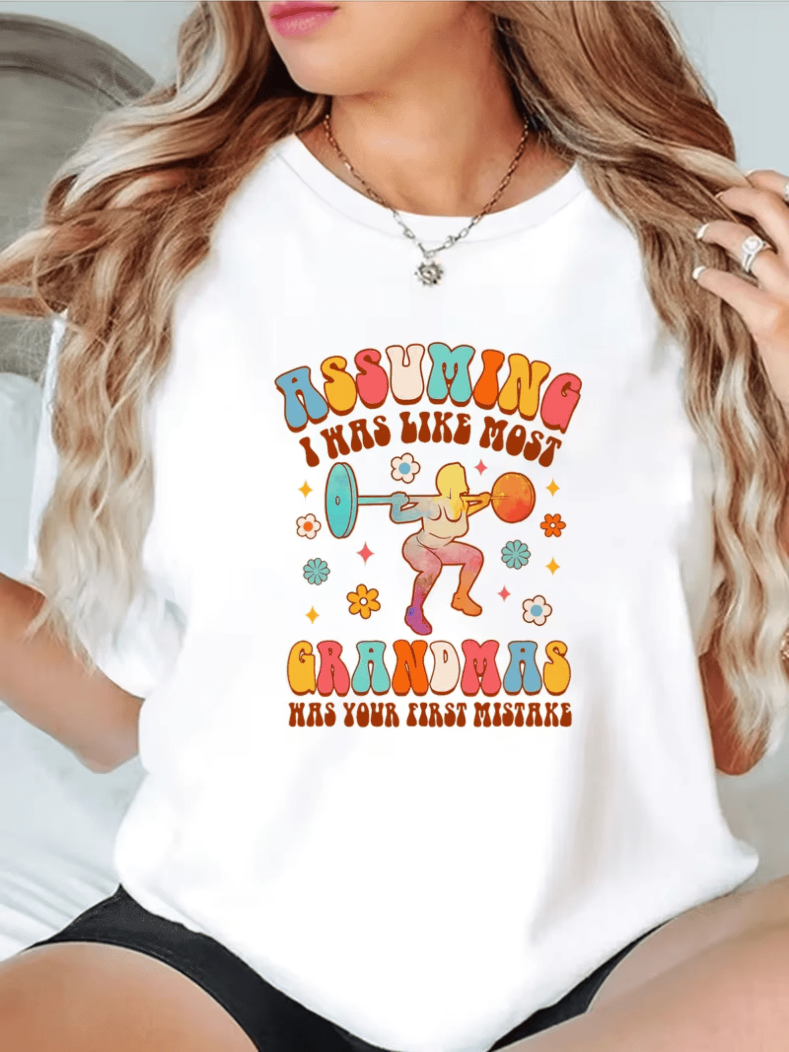 Colorful Illustration Depicts A Strong Grandmother Lifting Weights Surrounded By Small Flowers, Symbolizing Energy, Joy, And Feminine Confidence. Comfortable, Modern, Casual Women's T-Shirt For Everyday Wear. - 白色 - 查看 1