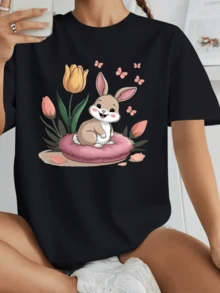 Conejo alegre sentado sobre un suave cojín rosado rodeado de tulipanes coloridos y pequeñas mariposas que simbolizan ternura esperanza y alegría camiseta de mujer casual cómoda y adorable ideal para uso diario - Negro - Ver 1