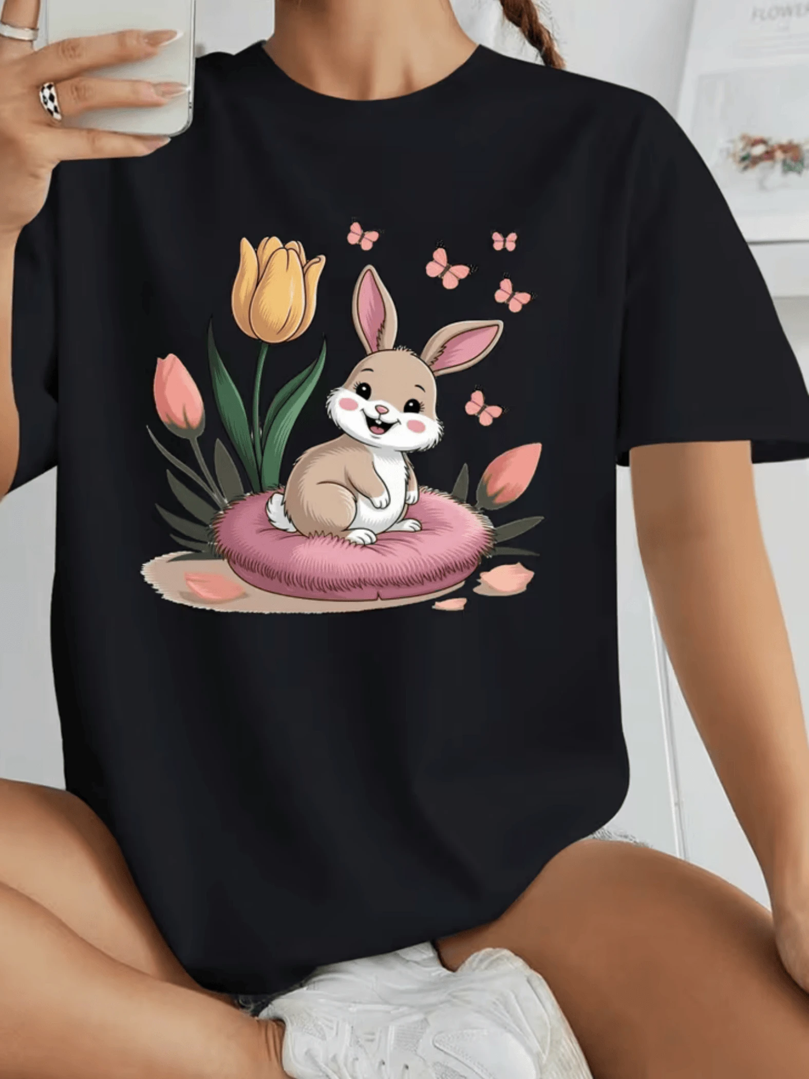 Conejo alegre sentado sobre un suave cojín rosado rodeado de tulipanes coloridos y pequeñas mariposas que simbolizan ternura esperanza y alegría camiseta de mujer casual cómoda y adorable ideal para uso diario - Negro - Ver 1