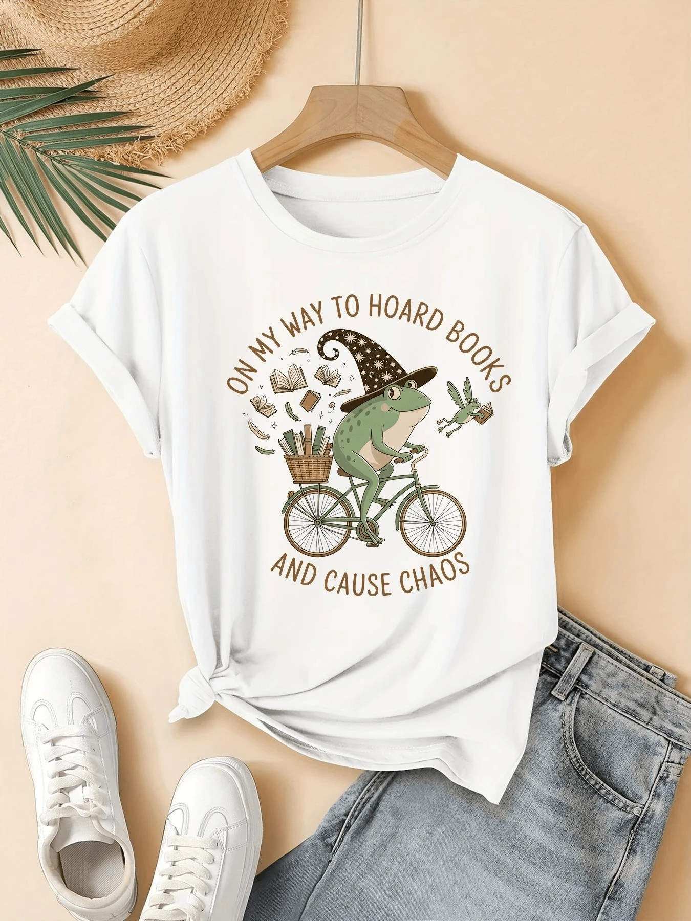 Rana con sombrero de mago montando una bicicleta entre libros voladores y hojas que simboliza la libertad creativa y la búsqueda mágica del conocimiento camiseta de mujer casual divertida para diario - Blanco - Ver 1