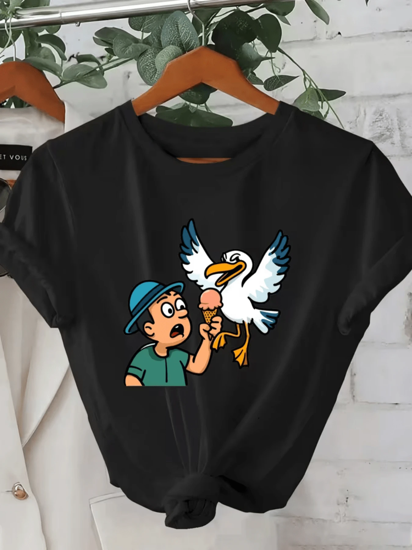 A Fun Drawing Shows A Surprised Young Man As A Mischievous Seagull Snatches His Ice Cream, Reflecting Humor And Summer Energy. A Casual And Comfortable Women's T-Shirt For Everyday Wear. - 黑色 - 查看 1