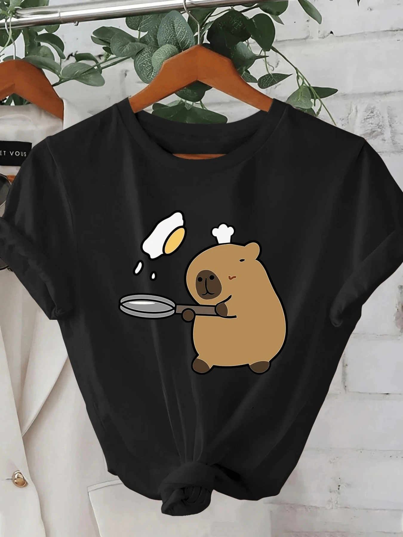 A Drawing Of A Cute Capybara Wearing A Chef's Hat Preparing An Egg In A Pan, Showing A Fun And Tender Scene Full Of Joy That Conveys Everyday Humor And Modern Charm. Comfortable Casual Women's T-Shirt For Daily Wear - 黑色 - 查看 1