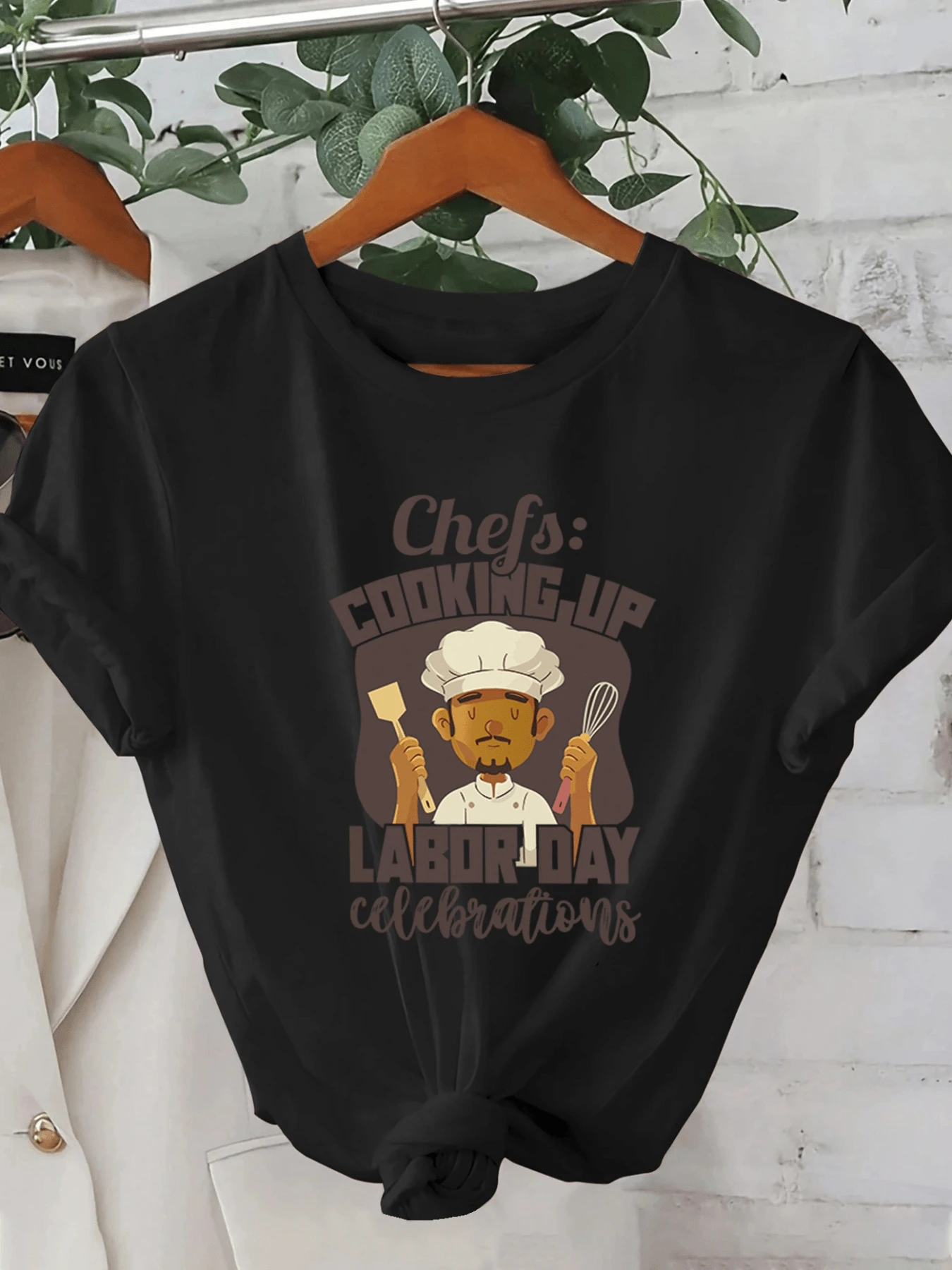 A Smiling Chef's Figure Holding Kitchen Utensils Celebrates The Spirit Of Work And Dedication In A Festive Atmosphere With A Motivational Message. A Modern, Comfortable, Casual Women's T-Shirt For Everyday Wear. - 黑色 - 查看 1