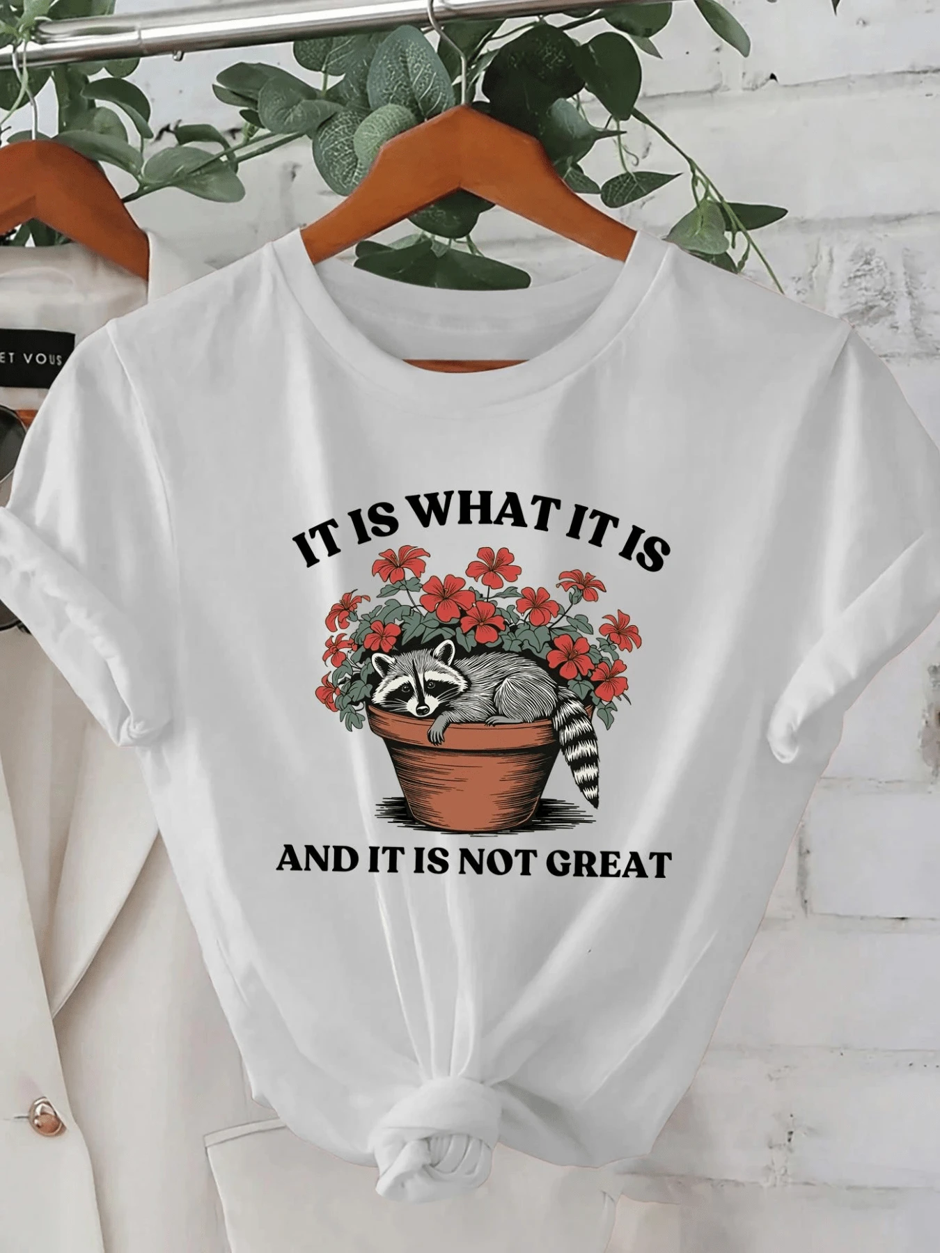 A Raccoon Resting In A Flowerpot Surrounded By Red Flowers Symbolizes The Blend Of Calm And Resignation In The Face Of Difficult Days. A Comfortable, Modern, Casual Women's T-Shirt For Everyday Wear. - 白色 - 查看 1