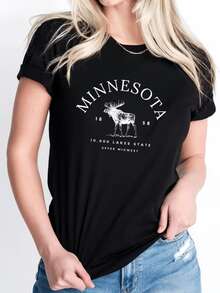 A Majestic Elk Figure Representing The Strength And Calm Of Minnesota's Natural Landscapes, Surrounded By Lettering That Evokes The Serenity Of The State Of Ten Thousand Lakes. A Comfortable, Casual Women's T-Shirt, Ideal For Everyday Wear. - 黑色 - 查看 1