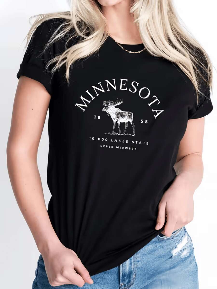 A Majestic Elk Figure Representing The Strength And Calm Of Minnesota's Natural Landscapes, Surrounded By Lettering That Evokes The Serenity Of The State Of Ten Thousand Lakes. A Comfortable, Casual Women's T-Shirt, Ideal For Everyday Wear. - 黑色 - 查看 1