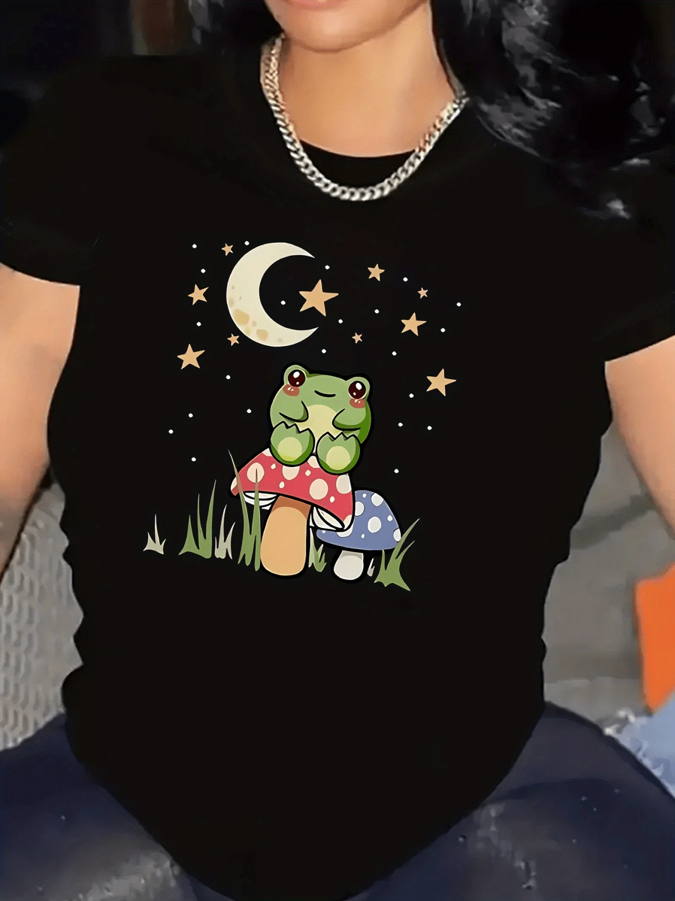 Rana verde con mirada tierna sentada sobre hongos de colores bajo una luna creciente rodeada de estrellas que evocan calma y fantasía camiseta de mujer casual cómoda para uso diario - Negro - Ver 1