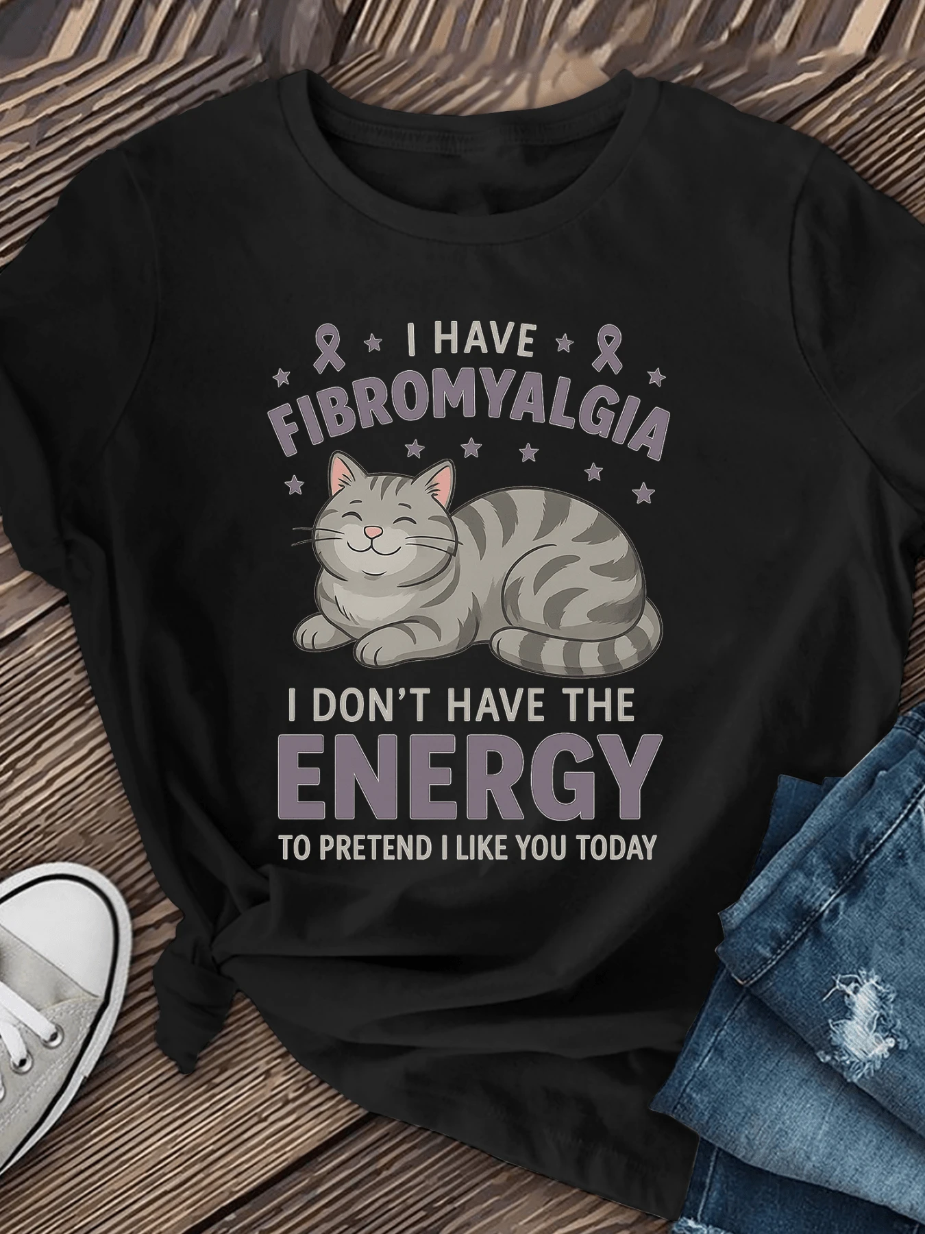 Smiling Gray Cat Resting Surrounded By Stars And Ribbons Symbolizing Strength Against Fibromyalgia With A Fun Message About Conserving Energy. Comfortable Casual Women's T-Shirt For Everyday Wear, Modern And Expressive. - Black - View 1