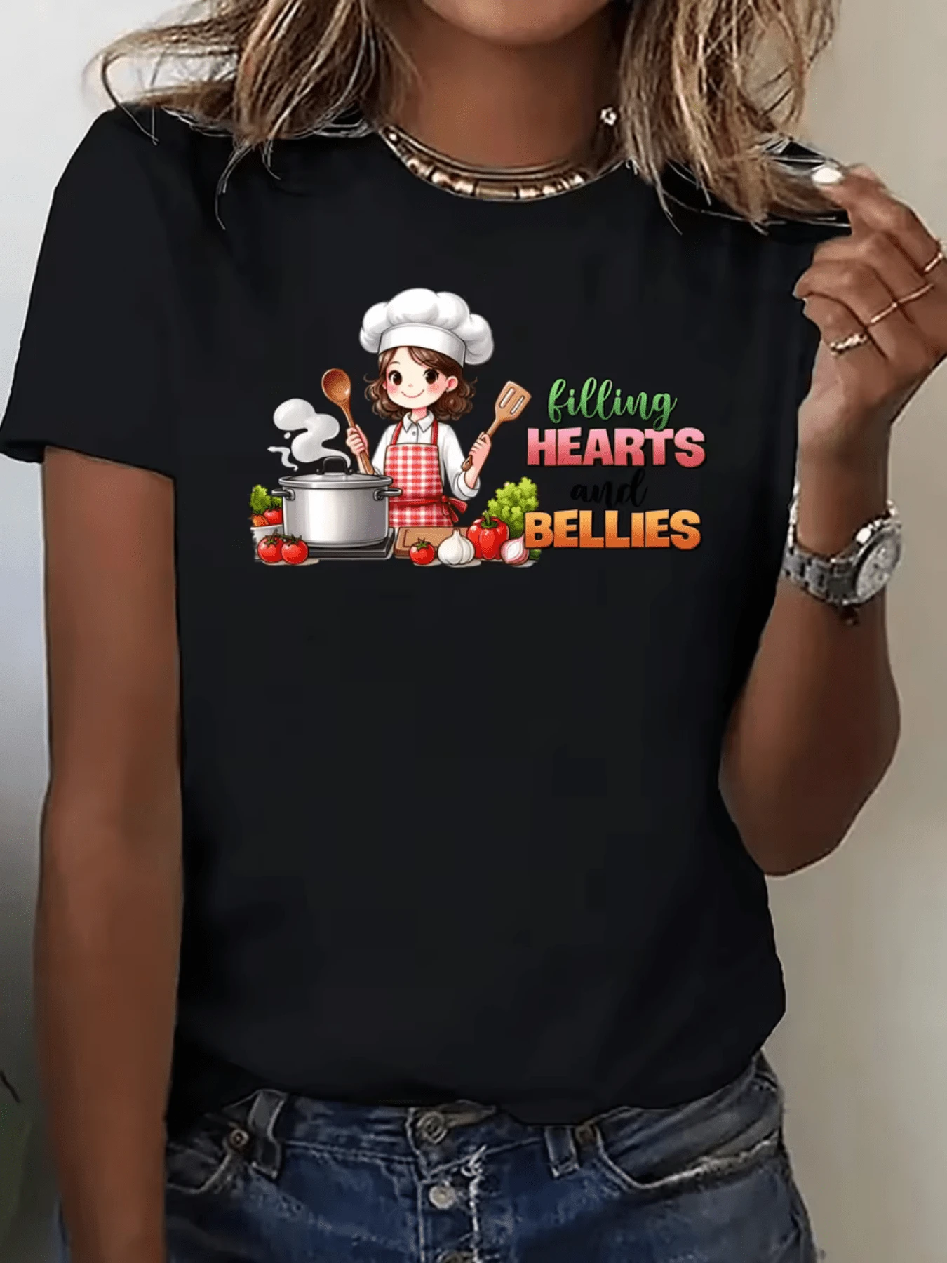 A Fun Scene Shows A Smiling Cook In A White Hat And Red Apron Surrounded By Fresh Vegetables, Pots, And Utensils, Conveying A Passion For Cooking And A Love For Sharing Warm Moments. A Modern, Casual Women's T-Shirt For Everyday Wear. - 黑色 - 查看 1
