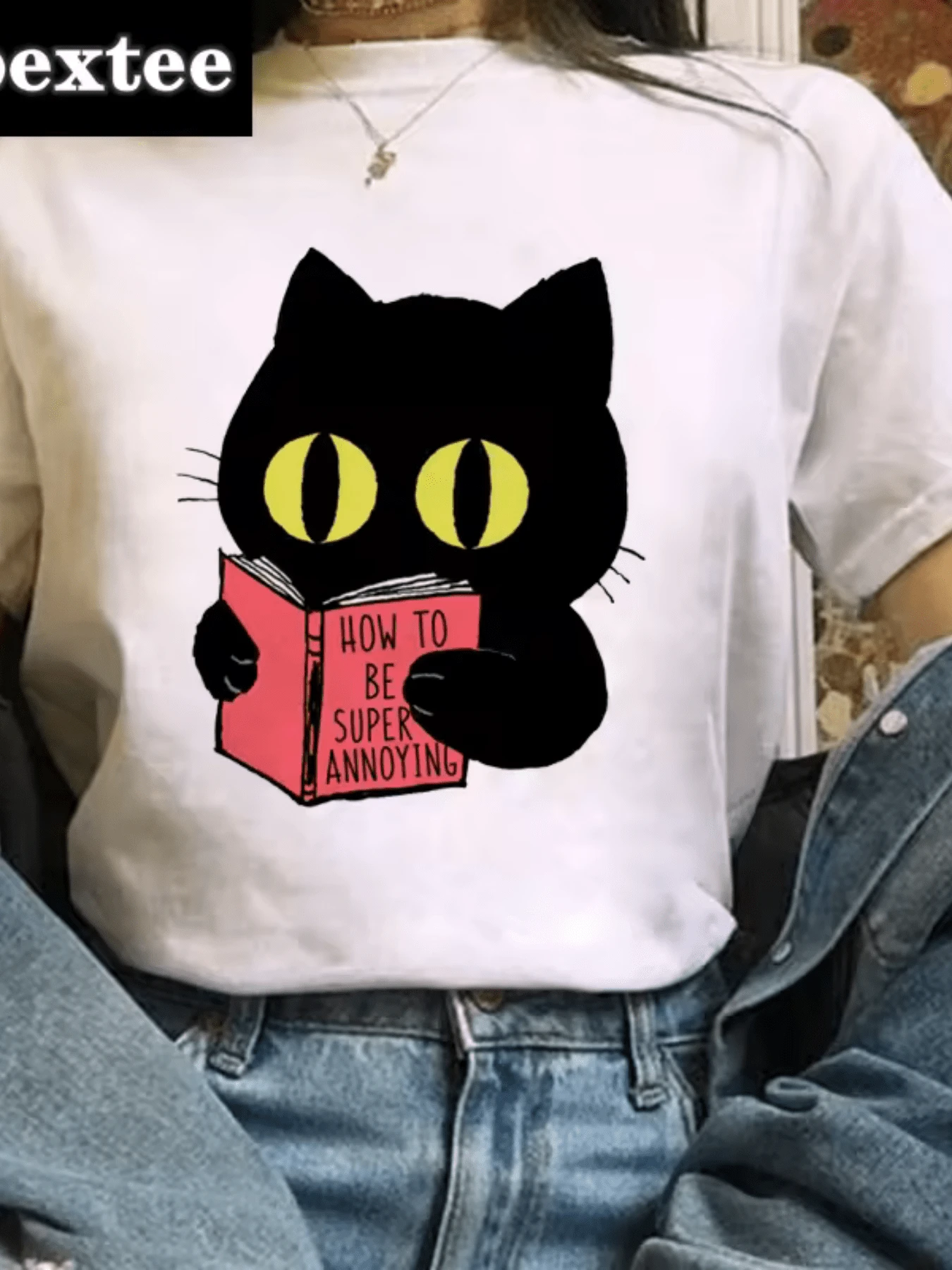 Gato con ojos amarillos que sostiene un libro rosado simbolizando humor travieso y curiosidad femenina en estilo moderno camiseta de mujer casual divertida para uso diario - Blanco - Ver 1