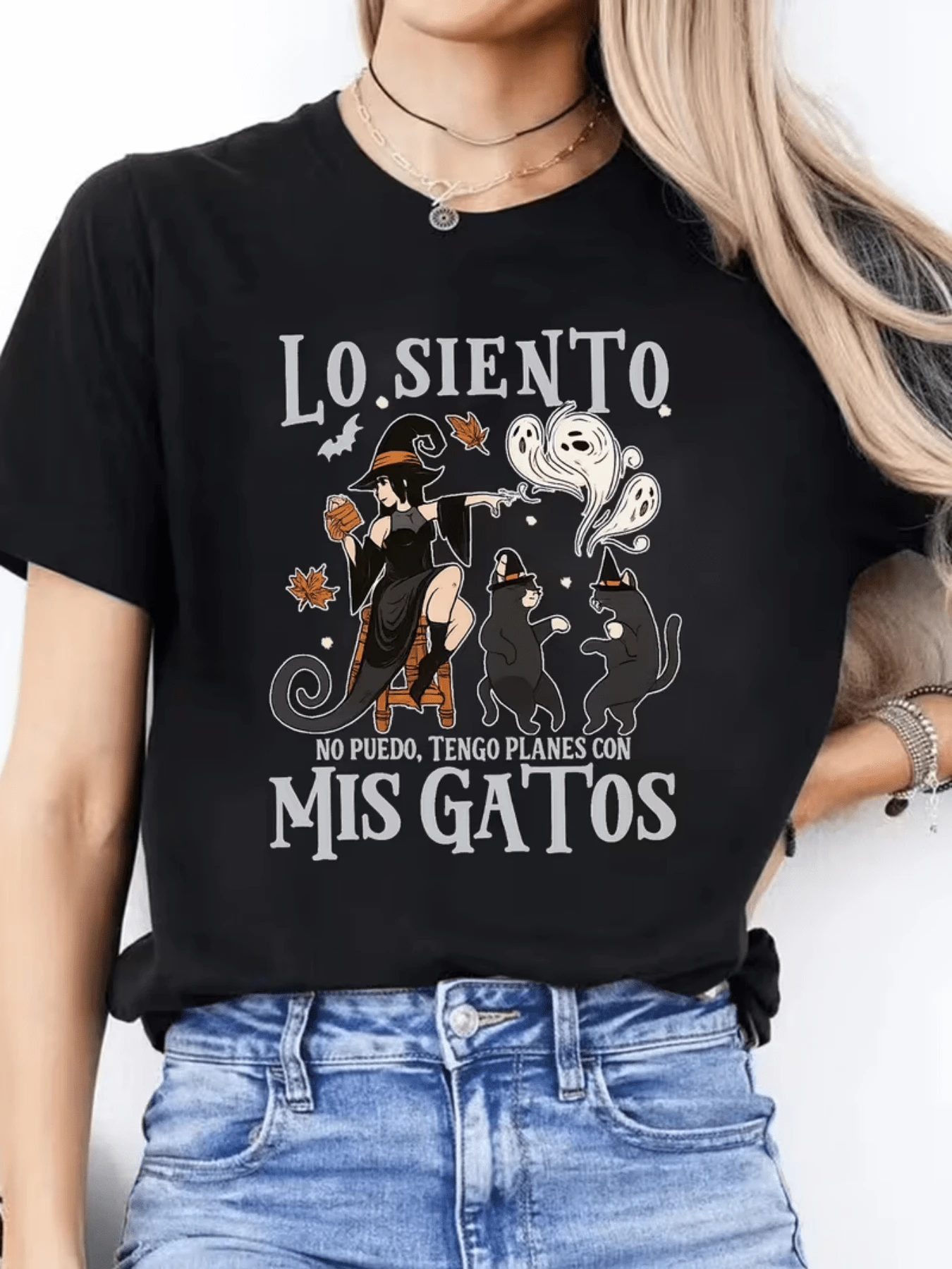 A Fun Scene With A Woman Dressed As A Witch Accompanied By Two Black Cats Under Autumn Leaves And Small Ghost Figures Symbolizing Love For Animals And Magical Humor. Comfortable Casual Women's T-Shirt For Everyday Wear - 黑色 - 查看 1