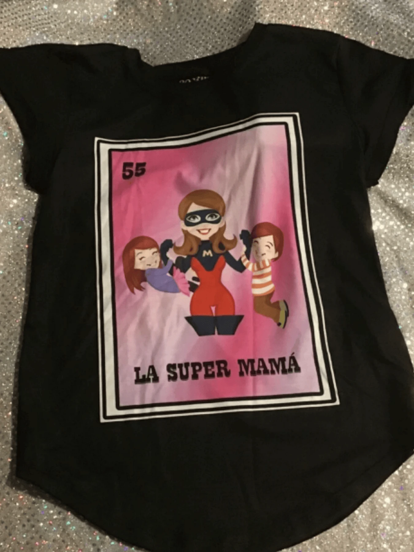 Mujer superheroína protegiendo a sus pequeños con valentía y amor representación del número 55 en la lotería mexicana celebrando la fuerza y dedicación de las madres. Camiseta de mujer con estampado vívido y único, ideal para un look casual y lleno de personalidad. - Negro - Ver 1