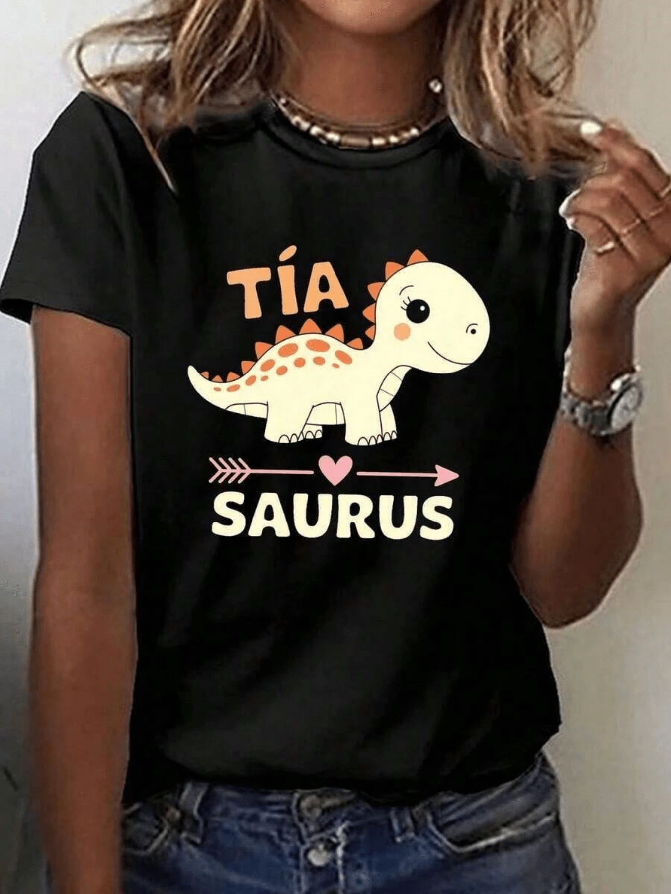 Un simpático dinosaurio sonriente con tonos suaves y pequeños detalles naranjas que transmiten alegría y ternura simboliza amor familiar y diversión camiseta de mujer casual cómoda para uso diario - Negro - Ver 1
